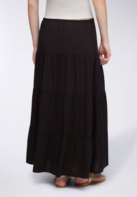Czarna, warstwowa spódnica maxi wykonana z miękkiego materiału, z elastycznym paskiem w talii i zwiewnym fasonem. Połączona z płaskimi, sandałami na ramiączkach.