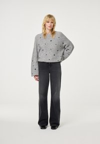 Grijze wollen trui met geborduurde donkerblauwe harten, gecombineerd met donkergrijze flared jeans. De outfit heeft een ontspannen pasvorm en een zachte textuur.