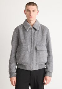 Gray herringbone-patterned jacket with a zip front, large flap pockets, and ribbed cuffs and hem. Made from textured fabric.