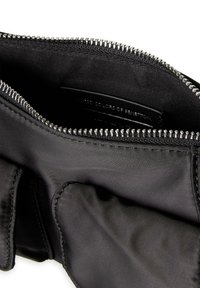 Czarna torba tekstylna w środku z metalowym zamkiem błyskawicznym. Charakteryzuje się gładkim, błyszczącym materiałem oraz widocznym ściegiem. Oznaczona napisem "United Colors of Benetton."