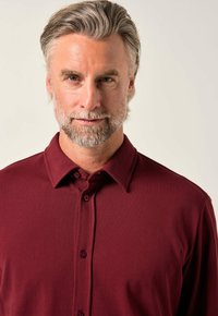 Polo shirt color marrone con colletto, tre bottoni e tessuto strutturato. La vestibilità è regolare, adatta per un abbigliamento informale.