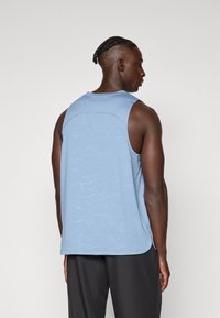 Lichtblauw mouwloos sporttop met een gestreept patroon, ronde halslijn en zijspleten, gecombineerd met donkere shorts.