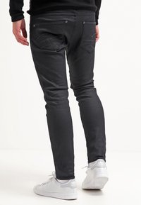 Zwarte denim jeans met een slim fit, voorzien van twee achterzakken en subtiele stikseldetails, gedragen met witte sneakers.