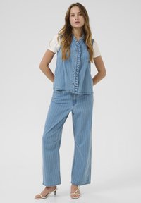 Svetle modrý denimový outfit s bezramínkovým topem s volány a širokými kalhotami s vertikálními bílými pruhy.