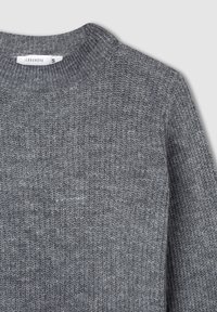 Szary prążkowany sweter z okrągłym dekoltem i małą białą metką rozmiaru "S" przy kołnierzu.