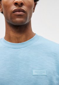 Sweatshirt azul-claro de gola redonda feito de um tecido suave, apresentando um pequeno rótulo retangular com o nome da marca no peito.