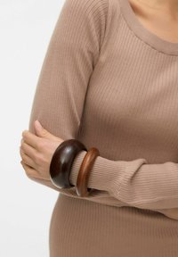 Divas koka aproces tumši un gaiši brūnā krāsā, valkātas uz kailas plaukstas. Valkātājs ir uzvilcis ribainu bēša krāsas topu, kas izceļ rotaslietas.