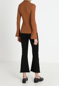 Top marron à manches longues côtelé avec des manches évasées, associé à un jean noir évasé. Les chaussures ont une forme lisse et arrondie avec un petit talon.