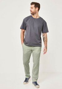 Graues T-Shirt mit kurzen Ärmeln, hellgrüne Hose und blaue Sneakers. Glattes Material, lockere Passform, Tattoos auf dem rechten Arm. Einfaches Design.