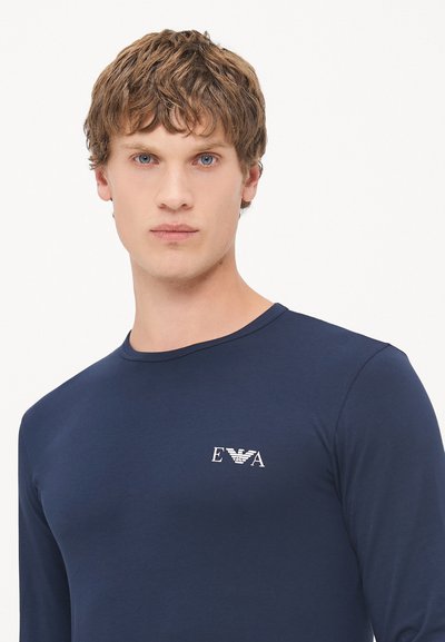 Navy langermet skjorte laget av mykt stoff, med en hvit logo på venstre bryst, rund hals og tettsittende design.