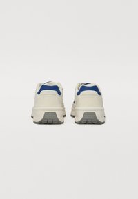 Baskets de sport blanches avec des accents bleus, une partie arrière texturée et une semelle épaisse grise. Elles ont un col rembourré et un matériau respirant.