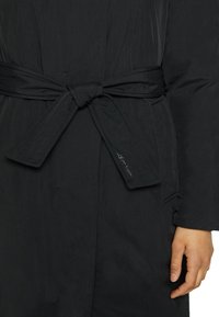 Abrigo de plumas negro con cintura ceñida, que presenta una superficie texturizada, mangas largas y un sutil logotipo en la cinta.