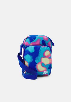 Bolso bandolera pequeño de Nike con patrones abstractos en azul, rosa y crema y una correa azul ajustable sobre un fondo blanco.