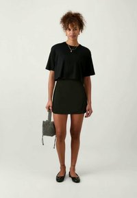 Svart cropped t-skjorte, svart miniskjørt, svarte flate sko og en liten svart-hvitt prikkete veske. Glatt stoff, komfortabel passform, enkelt design.