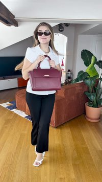 Bordeaux håndtaske med dobbelte top-håndtag, rektangulær form, glat tekstur og forlommer. Modellen bærer en hvid top og sorte bukser.