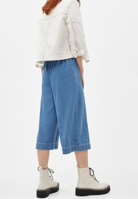 Ljus denim culotter med vida ben, med en kortad längd och rullad fåll, kombinerade med krämfärgade ankelboots med svarta sular och snörning.