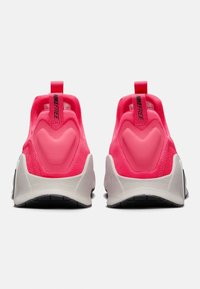 Różowe buty sportowe z bezszwową cholewk�ą, zaokrąglonym piętą, teksturowanym materiałem i kontrastującą białą podeszwą. Posiadają pętle do zakładania z tyłu.
