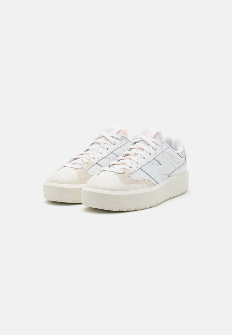 Baskets blanches avec des accents en suède gris et beige, design à lacets, et une semelle épaisse et texturée. Comprend un logo sur la languette et sur le côté.
