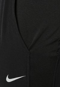 Black athletic tank top featuring a deep V-cut design, fitted texture, and white Nike logo at the bottom left corner.