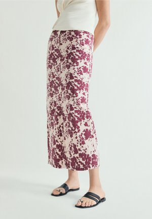 Mujer con pantalones anchos hasta el tobillo con estampado floral morado, camiseta blanca sin mangas y sandalias planas negras con detalles plateados.
