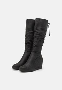 Bottes à plateforme compensée noires au design décontracté, en cuir texturé, de hauteur mi-mollet avec un bout arrondi. Agrémentées d'un détail de lacet.