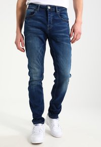 Mörkblå jeans med slim fit, med subtila blekningar och en klassisk fem-fickorsdesign. Tillverkade av denim med synlig sömnad och metallfästen.