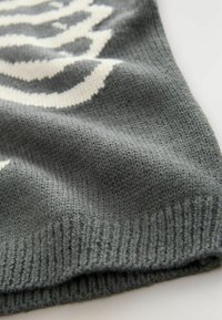 Grå strikket stof med en ribbet tekstur, prydet med et hvidt abstrakt mønster. Stoffet er blødt og har en let stræk.