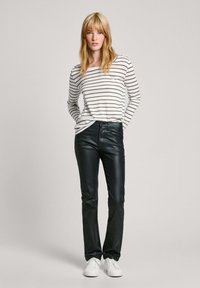 Pantalones de cuero negro de corte slim combinados con una camisa de manga larga blanca a rayas. El conjunto se completa con zapatillas blancas.