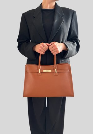 Bruine leren handtas met een textuur oppervlak, twee stevige handvatten en een gouden sluiting. Gedragen met een zwarte blazer en top.