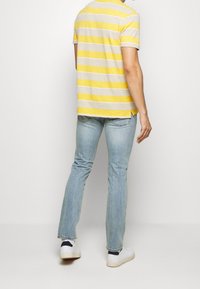 Camiseta de manga corta a rayas en amarillo y gris, combinada con unos vaqueros de denim azul claro. Los vaqueros son rectos y tienen una textura desgastada.