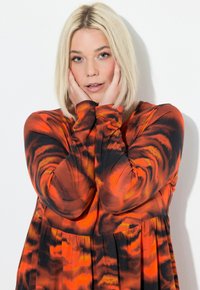 Langärmliges Kleid in einem abstrakten Muster aus Orange, Schwarz und Rot. Weicher Stoff mit lockerer Passform und gerafftem Taillendetail, das eine fließende Silhouette kreiert.