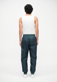 Sportoutfit mit einem weißen Tanktop und dunkelgrünen, glänzenden Jogginghosen mit elastischem Bund und Bündchen, von hinten präsentiert.