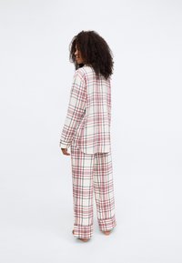 Conjunto de ropa cómoda de cuadros en colores crema, rojo y azul marino; incluye una camisa de corte holgado y pantalones a juego con piernas anchas y textura suave de algodón.