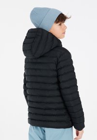 Chaqueta acolchada negra con diseño de acolchado horizontal y capucha. El modelo lleva un gorro de canalé azul claro. El fondo es blanco liso.