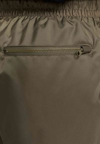 Kabatas ar rāvējslēdzēju uz haki auduma, ar strukturētu rāvējslēdzēju vilkšanu un elastīgu jostu, ar gludu, nedaudz spīdīgu virsmas tekstūru.