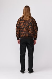 Brun camouflage quiltet bomberjakke med ribbede manchetter og kant, parret med sorte bukser og sorte sko. Set fra ryggen.