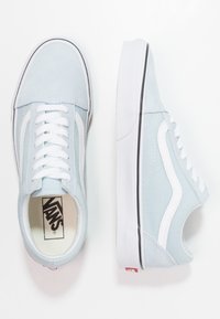 Lys blå joggesko laget av lerret med hvite detaljer og snørebånd. Har en gummisåle med en subtil svart stripe langs kanten. Vans-logoen synlig.
