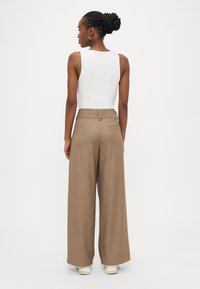 Brūnas platās bikses no teksturēta auduma, kombinētas ar baltu bezroku topu. Aprīkotas ar piegrieztu jostasvietu un aizmugurējām kabatām.