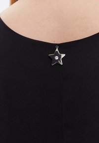 Prenda negra con escote redondeado y un broche metálico en forma de estrella adornado con un rhinestone transparente, que añade un acento decorativo.