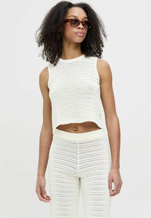 Weißes, kurzes Tanktop mit strukturiertem, gestricktem Muster, kombiniert mit passenden, eng anliegenden Hosen, die beide einen gerippten Bund und Saum aufweisen.