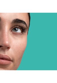 Zbliżenie na twarz o gładkiej cerze, wyraźnych rzęsach i niebieskim oku, na tle jednolitego turkusowego koloru.