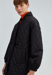 Giubbotto imbottito nero con colletto alto, vestibilità comoda, spalle calate e polsini a coste. Presenta tasche laterali e una texture a motivo diamante.