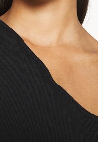 Black ribbed top with an asymmetric neckline, featuring a textured fabric and a close fit, highlighting the décolletage area.