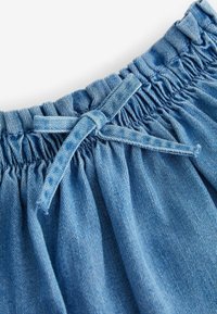 Ceinture élastique avec un cordon en denim noué sur un tissu bleu clair froncé, montrant un détail en gros plan d'un pantalon ou short décontracté.