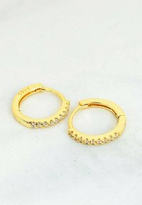 Pendientes de aro dorados con un acabado liso y pulido, adornados con una fila de pequeñas piedras brillantes a lo largo del borde exterior. Cierre ajustable.