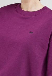 Purple sweatshirt made of cotton blend, featuring a ribbed crew neck and small embroidered "Lee" logo on the chest. Smooth texture.