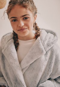 Accappatoio grigio chiaro, morbido e con cappuccio, dalla texture soffice. Presenta un colletto a scialle e un design avvolgente, per aumentare comfort e calore.