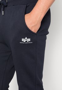 Marineblå bomulds joggers med snor i livet, sidelommer og et hvidt logo på venstre lår. Blød tekstur og afslappet pasform.