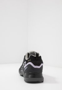 Musta vaelluskengät, joissa on kankainen pintamateriaali, harmaat yksityiskohdat, vedenpitävä GORE-TEX-merkki ja kestävä kumipohja. Matala profiili.