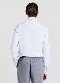 Camicia azzurra a maniche lunghe con colletto classico e polsini con bottoni, abbinata a pantaloni grigi con cintura elastica e tasche posteriori.